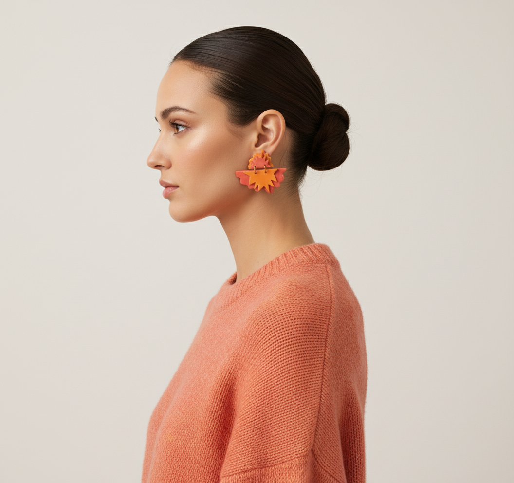 Editorial fashion photo of model wearing coral-orange maple leaf earrings